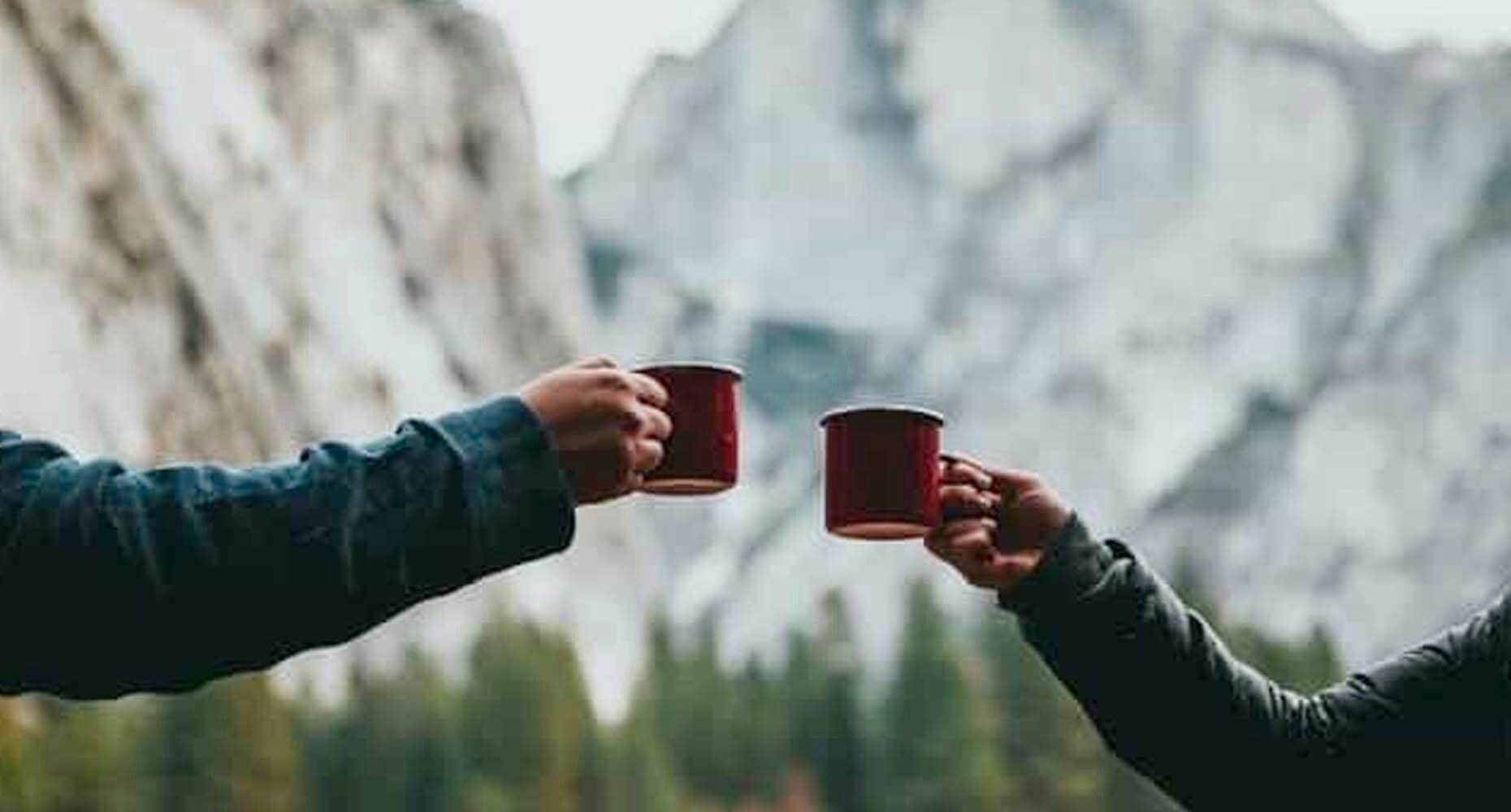 hands colding coffee cups in front of mountains