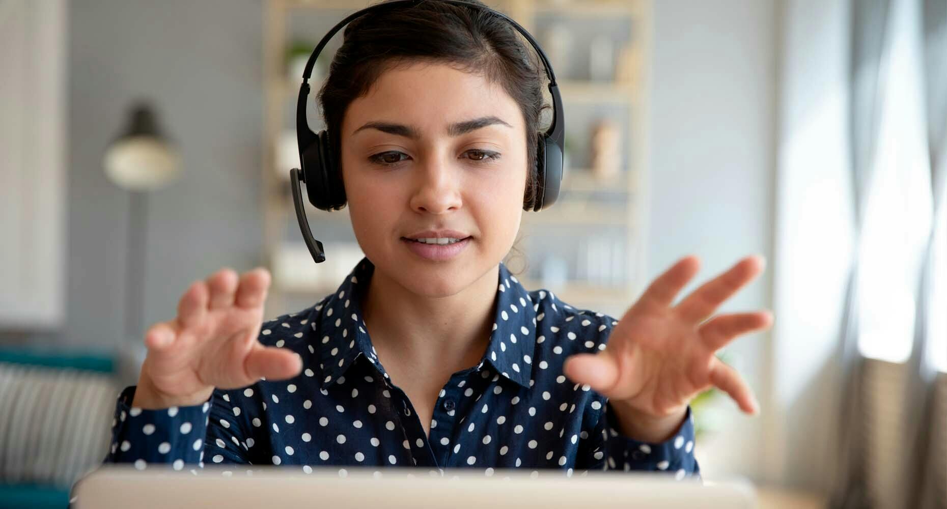 Woman with a headset on gesticulating at her computer screen